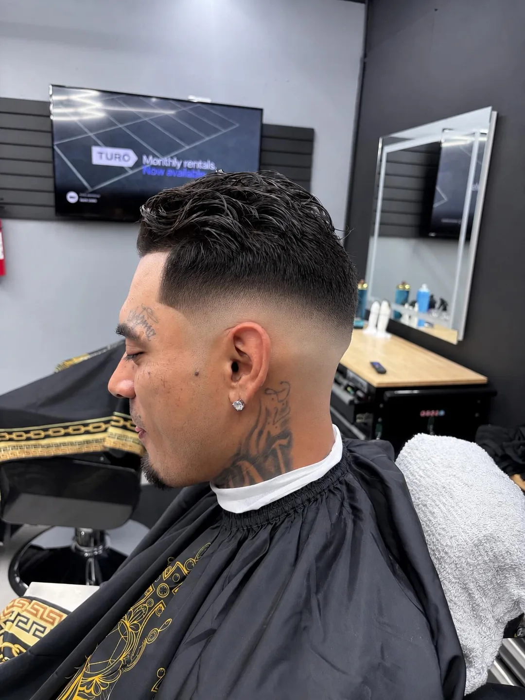Man getting a fade haircut in a barbershop, seated in profile with a cape on and a mirror behind him