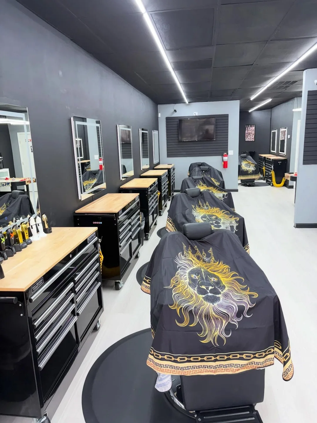 Row of barber stations with a black and gold lion-print cape draped over a chair