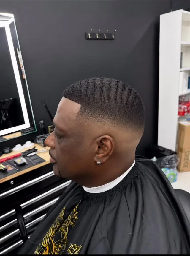 Man getting a fresh fade haircut in a barbershop, seated beside a mirror and tool drawers